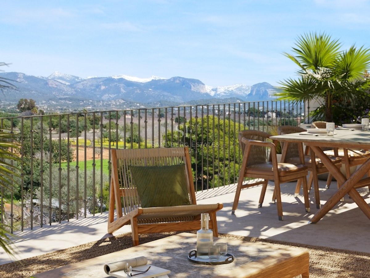 Sunny terrace with wooden furniture and rug overlooking a valley and snow-capped mountains.