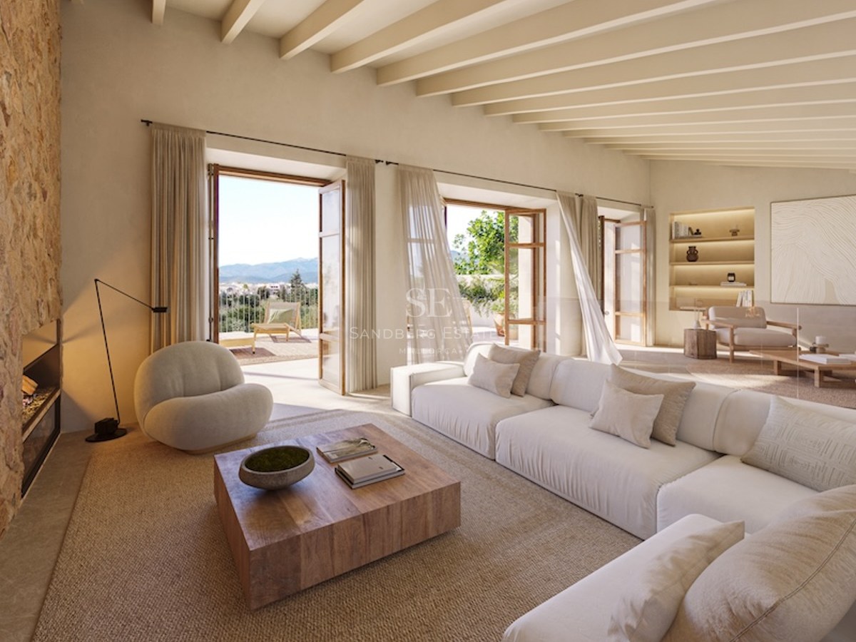 Bright living room with white sofa, stone fireplace, wooden beams, and open doors to a sunny terrace.