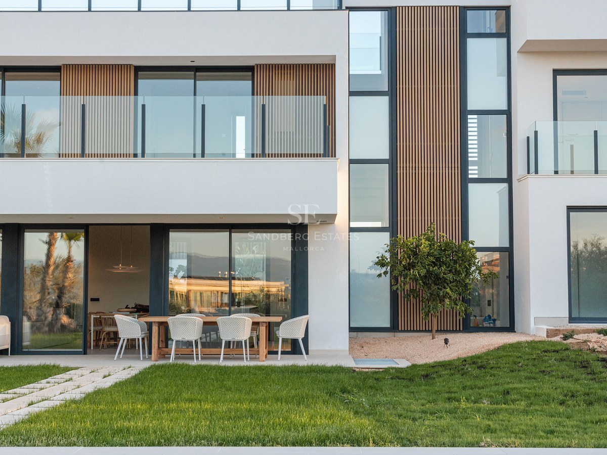 Modern white villa with wood accents, large windows, and a turquoise swimming pool in front of a green lawn.