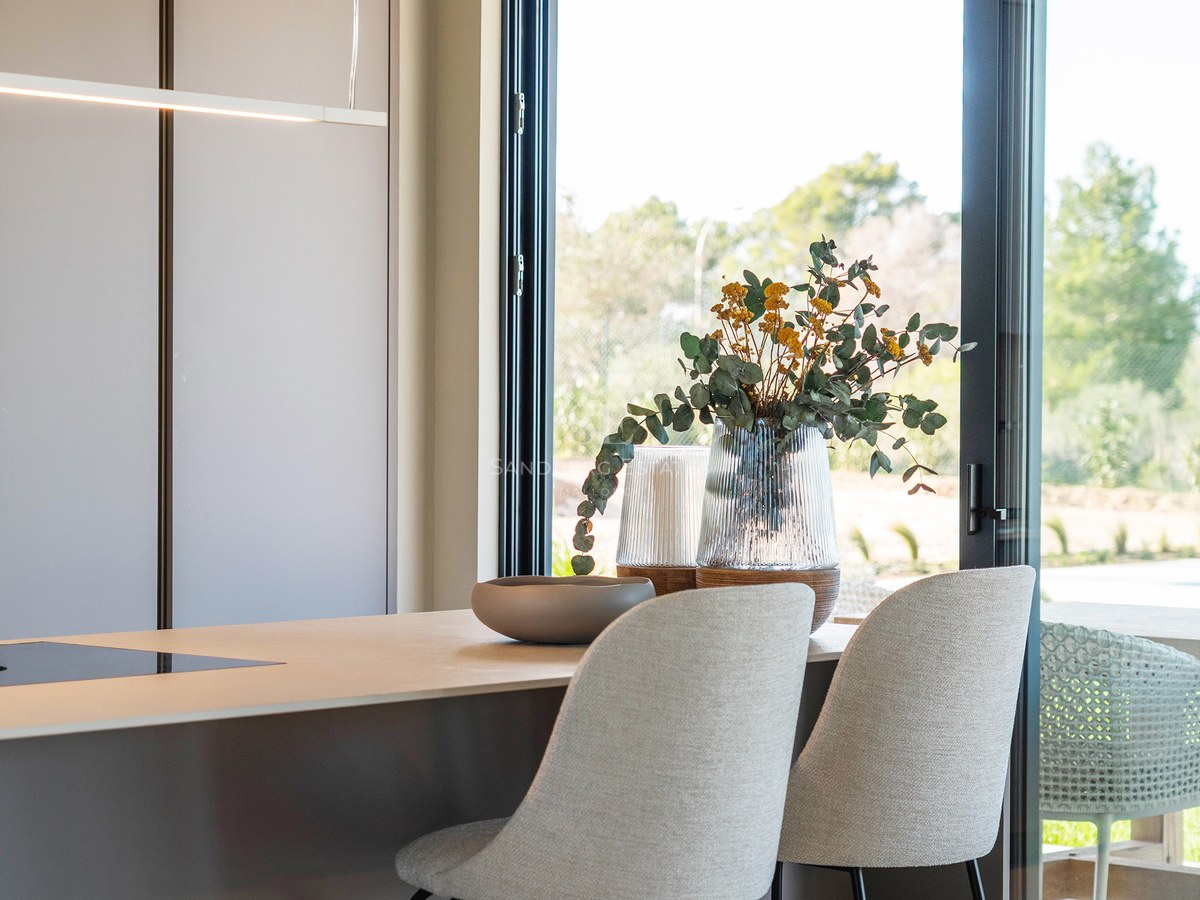 Modern kitchen island with grey bar stools next to a large glass door overlooking a garden.