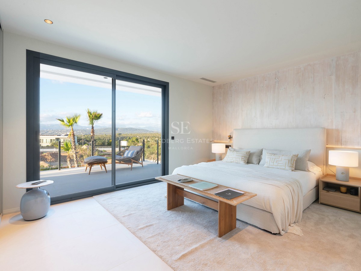 Luxury bedroom with white bed, wood accent wall, and glass door opening to a terrace with mountain views.