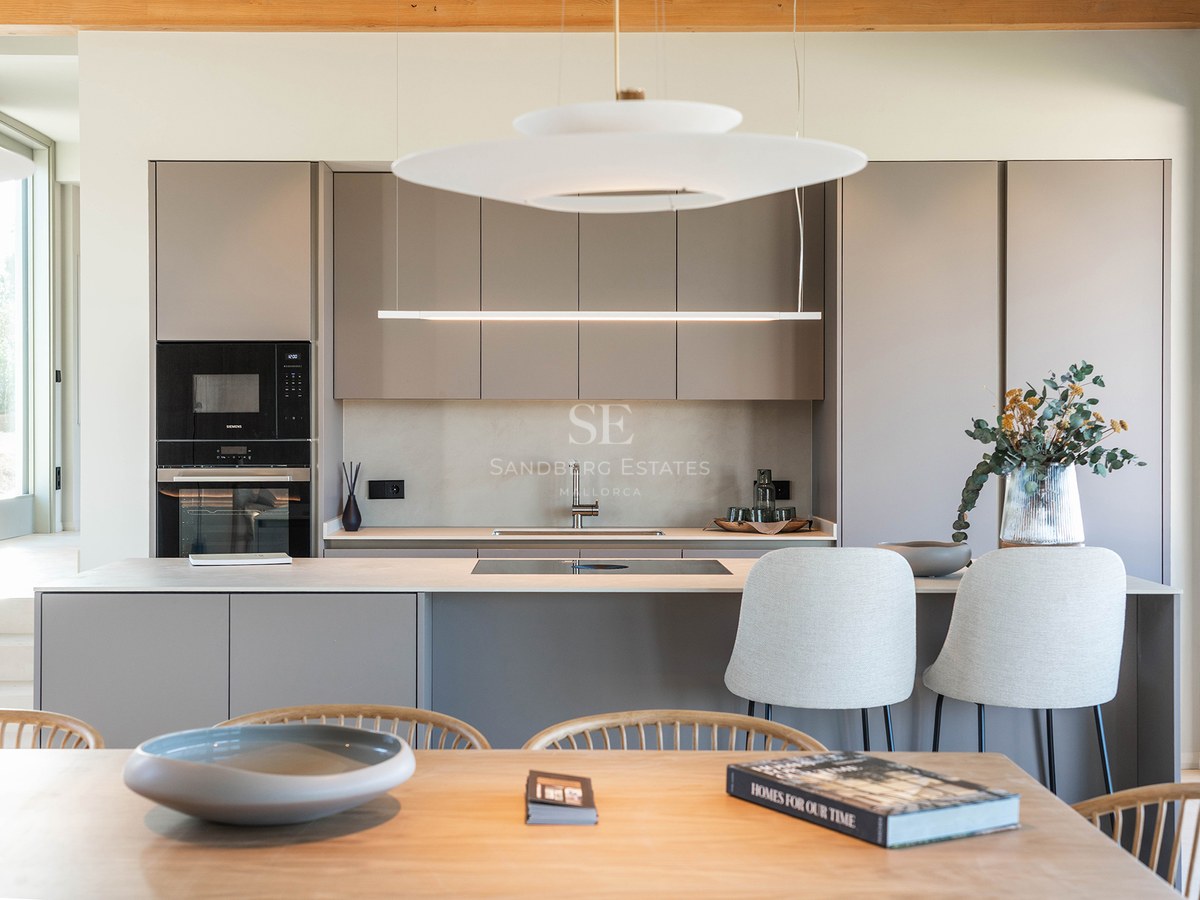 A contemporary kitchen featuring taupe handleless cabinets, a central island with stools, and elegant pendant lights.