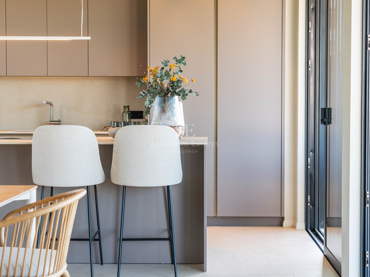 A modern kitchen featuring matte taupe cabinets, an island with two light-colored bar stools, and a wooden ceiling beam.
