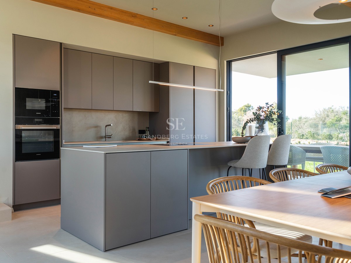 Minimalist kitchen with taupe island, integrated appliances, and wooden dining table under exposed beams.
