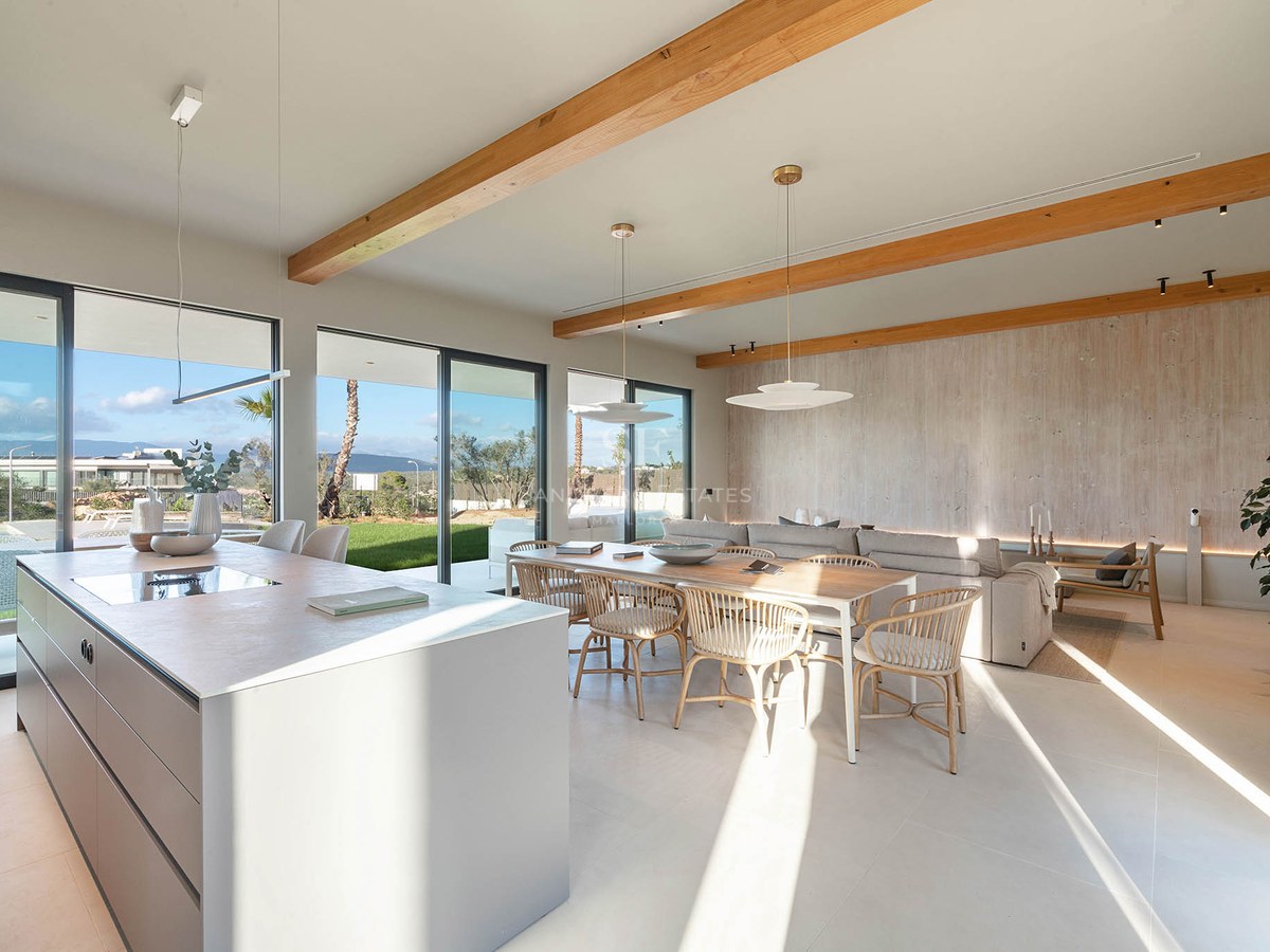 Spacious open-plan living room featuring wooden ceiling beams, kitchen island, dining area, and large glass doors to garden.