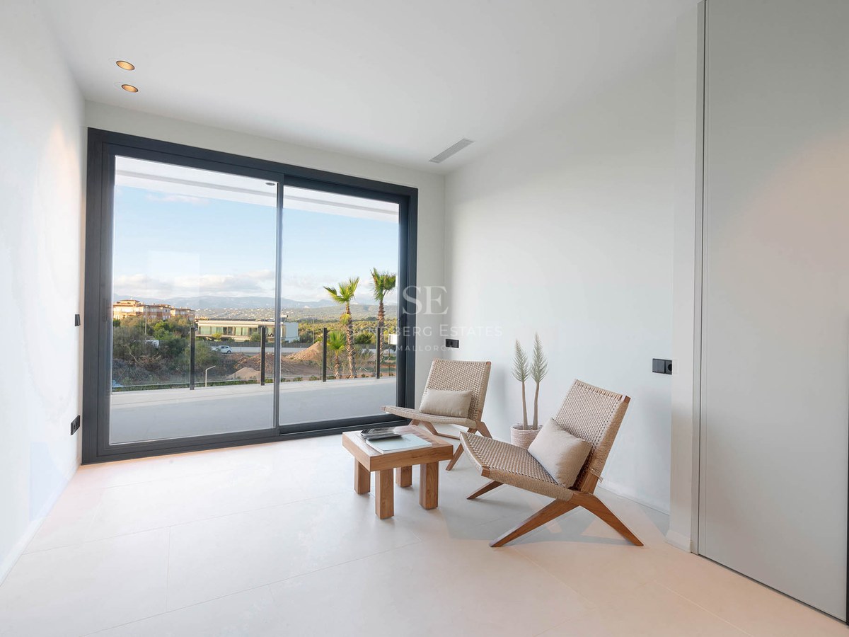 Minimalist white room featuring two design chairs, a wooden table, and large sliding glass doors overlooking a landscape.