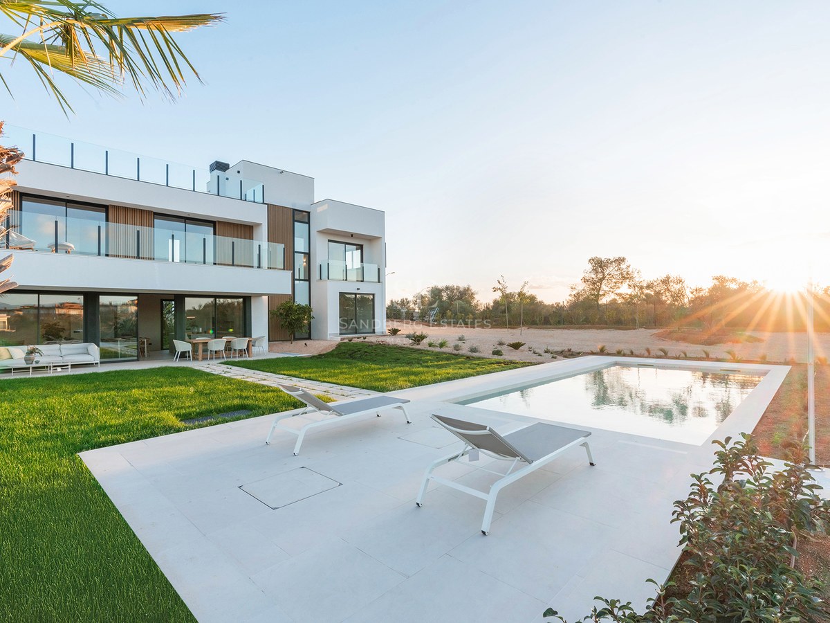 Modern white two-story villa with a swimming pool, sun loungers, and green lawn under a golden sunset sky.