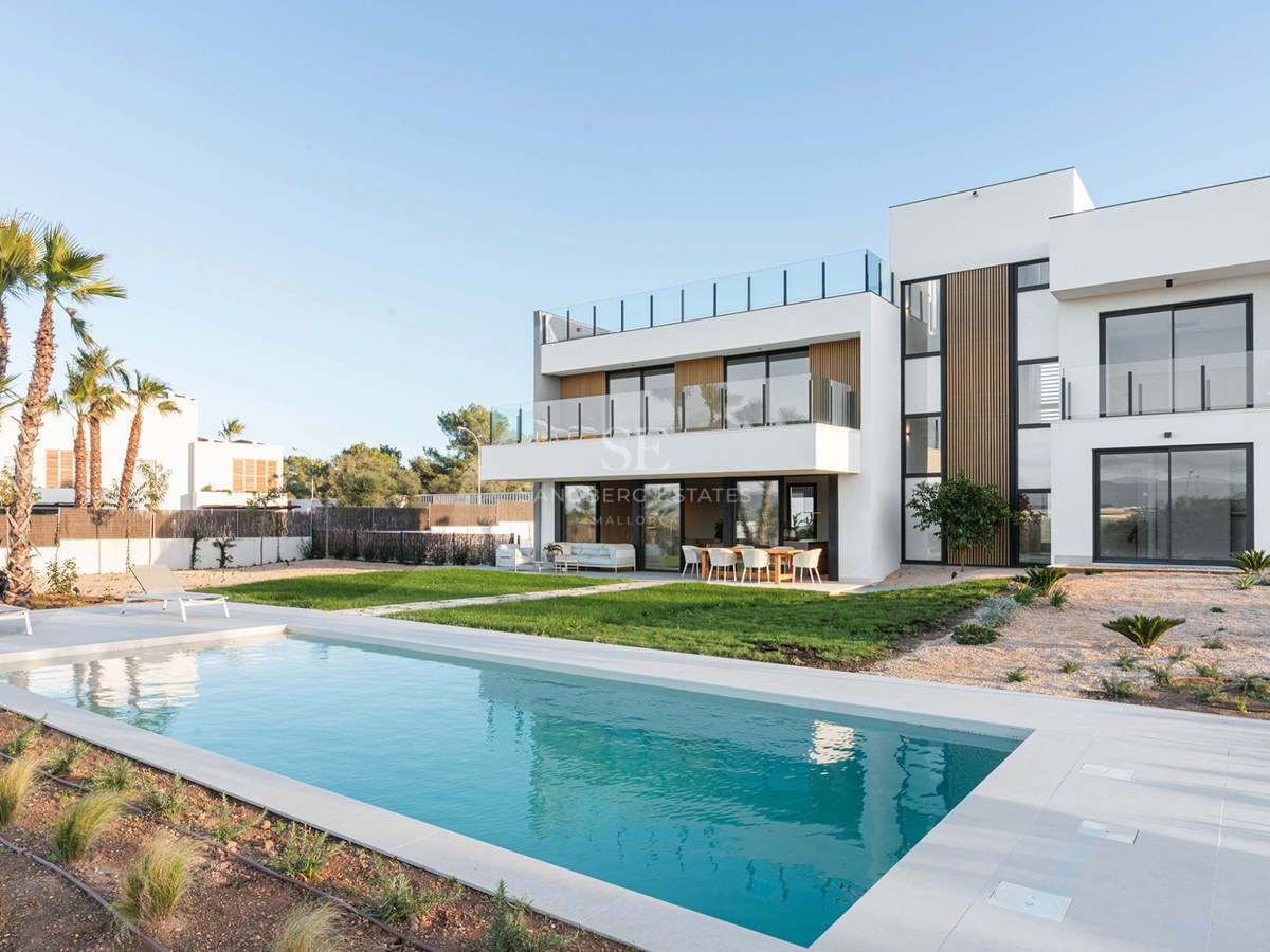 Modern white design villa featuring a rectangular swimming pool, manicured lawn, and spacious terraces under a clear sky.