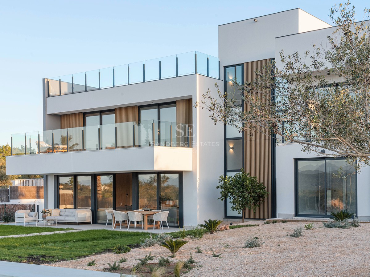 Two-story modern white villa with glass balconies, wooden slats, outdoor dining area, and a rooftop terrace.