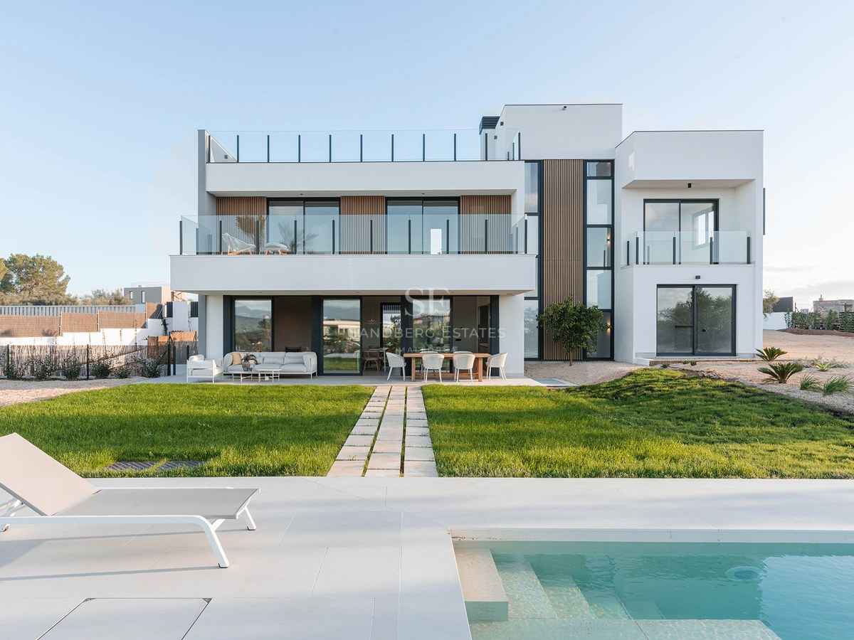 Modern white two-story villa with a turquoise swimming pool, sun lounger, and a green lawn under a clear sky.