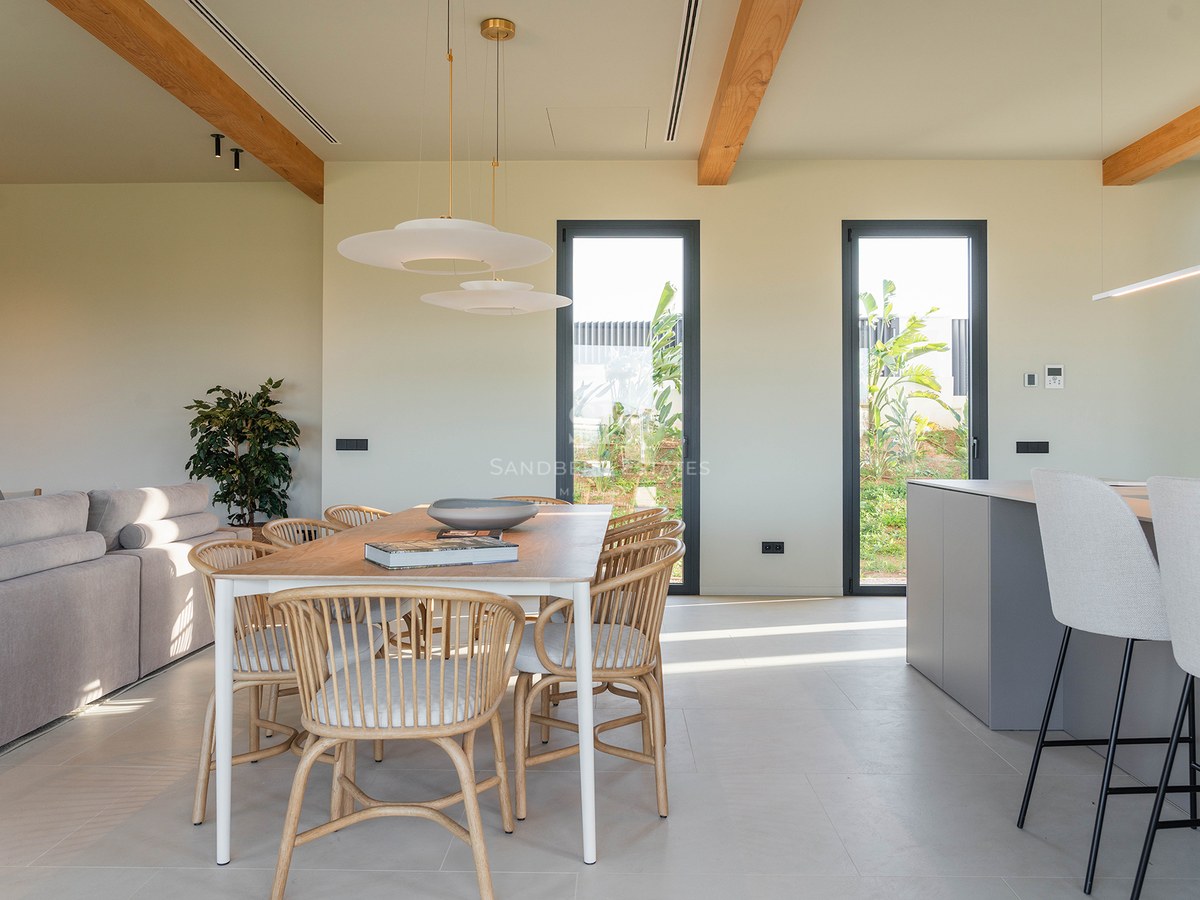 Bright dining room featuring a wooden table, designer chairs, and exposed wooden ceiling beams.