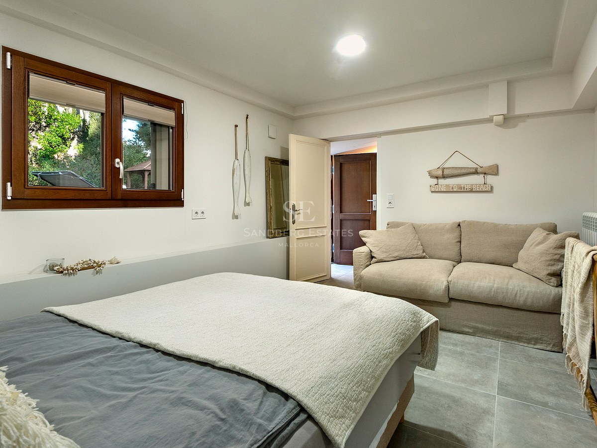 Un dormitorio luminoso con una cama gris, un sofá beige, una ventana de madera y decoración de temática náutica.