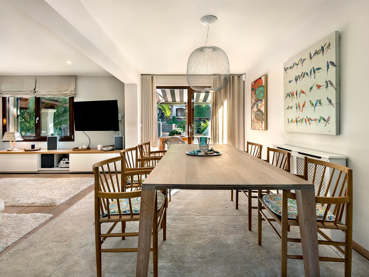 Mesa de comedor de madera con sillas bajo una lámpara colgante esférica, abierta al salón y la terraza.