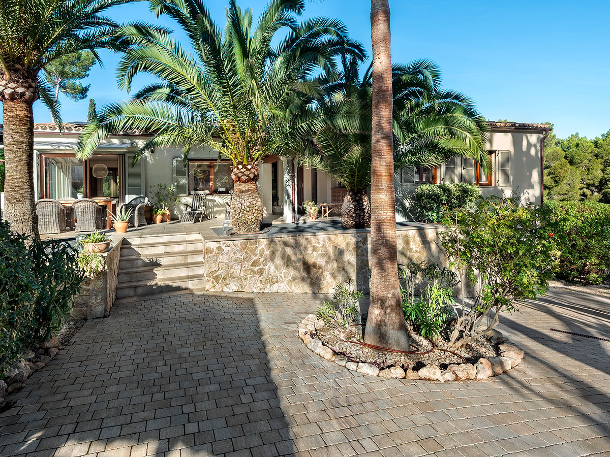 Exterior de una casa mediterránea con muros de piedra y grandes palmeras bajo un cielo azul.
