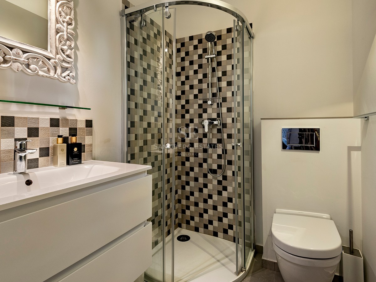 Baño moderno con ducha de vidrio, azulejos en damero, lavabo blanco y un espejo con marco blanco ornamentado.