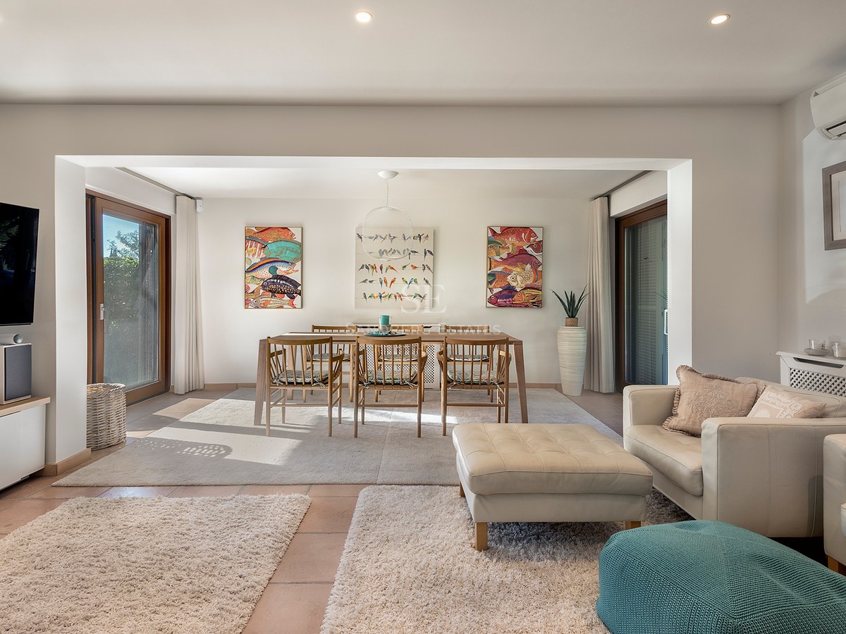 Sala luminosa de planta abierta con sofás de cuero crema, mesa de comedor de madera y arte de peces coloridos.