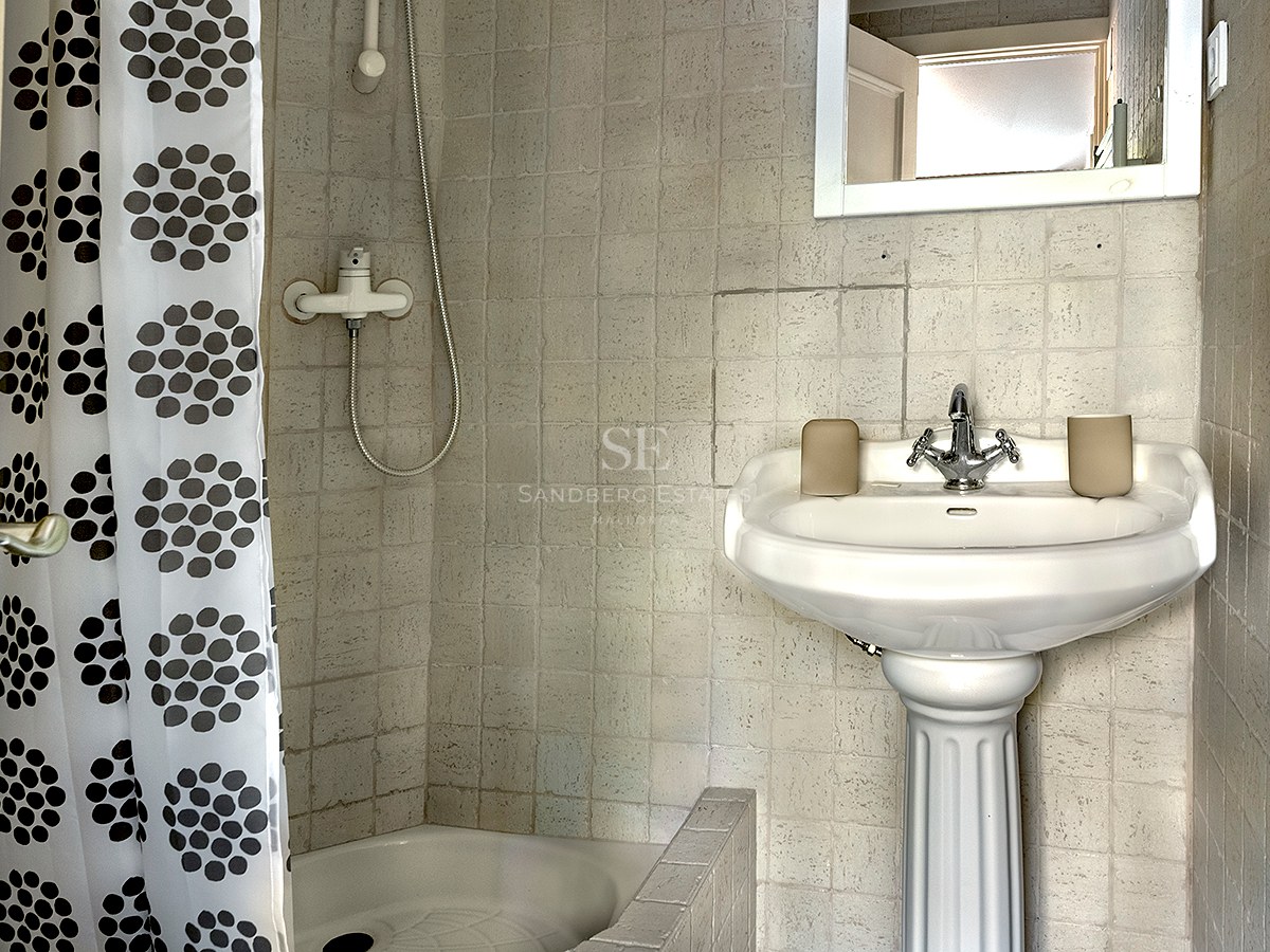 Baño pequeño con lavabo de pedestal blanco, paredes alicatadas y ducha con cortina de círculos.
