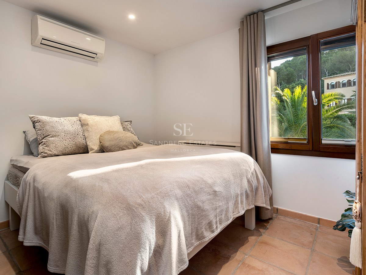 Dormitorio con cama doble, suelos de terracota, aire acondicionado y ventana con vistas a palmeras.