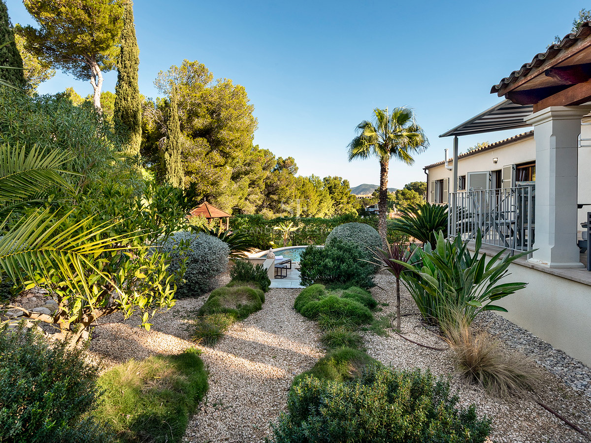 Jardín exuberante con caminos de grava que conducen a una piscina junto a una villa de estilo mediterráneo.