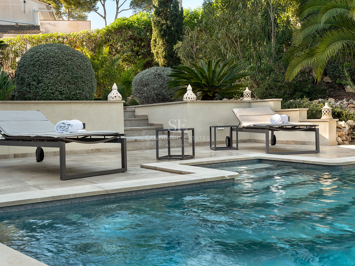 Piscina de aguas azules con tumbonas modernas en una terraza de piedra rodeada de vegetación mediterránea.