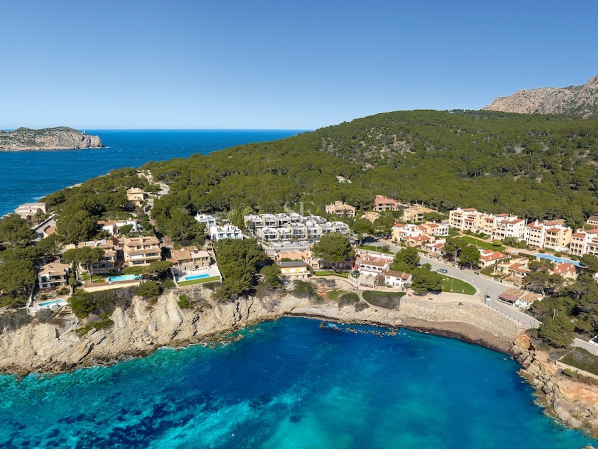 Vista aérea de villas mediterráneas en un acantilado sobre una bahía turquesa y bosque verde.