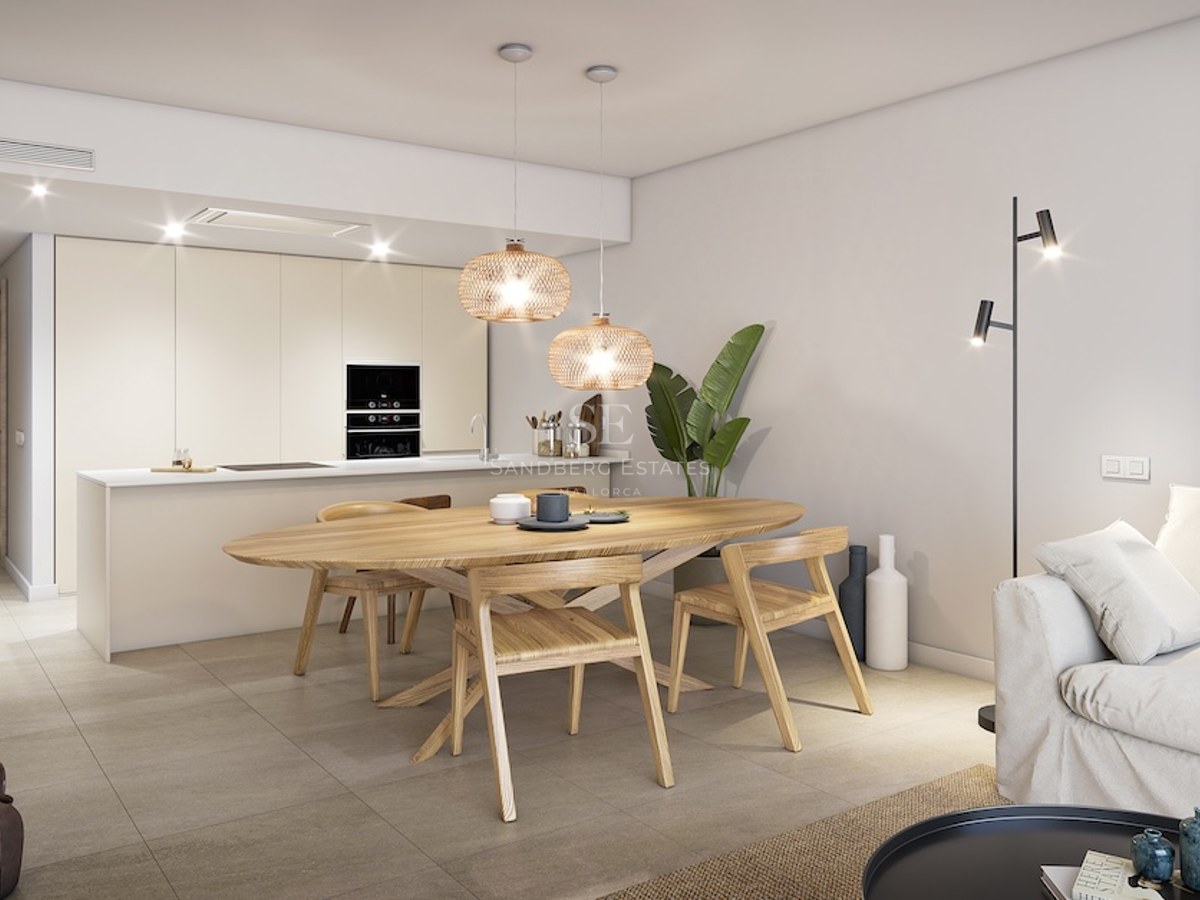 Comedor moderno con mesa de madera ovalada, lámparas de mimbre colgantes y cocina minimalista al fondo.