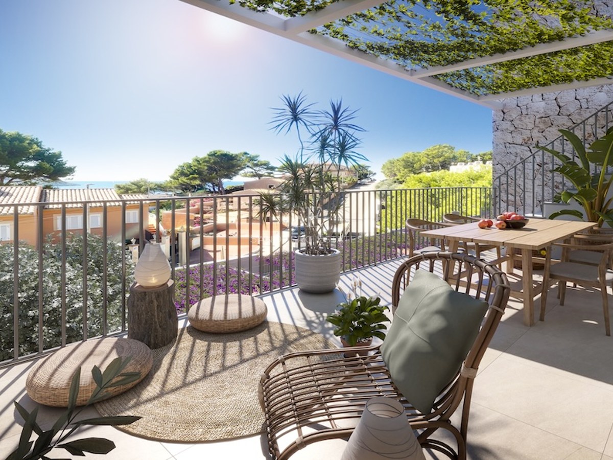 Terraza soleada con mesa de comedor de madera, silla de ratán y pérgola con plantas frente al mar.