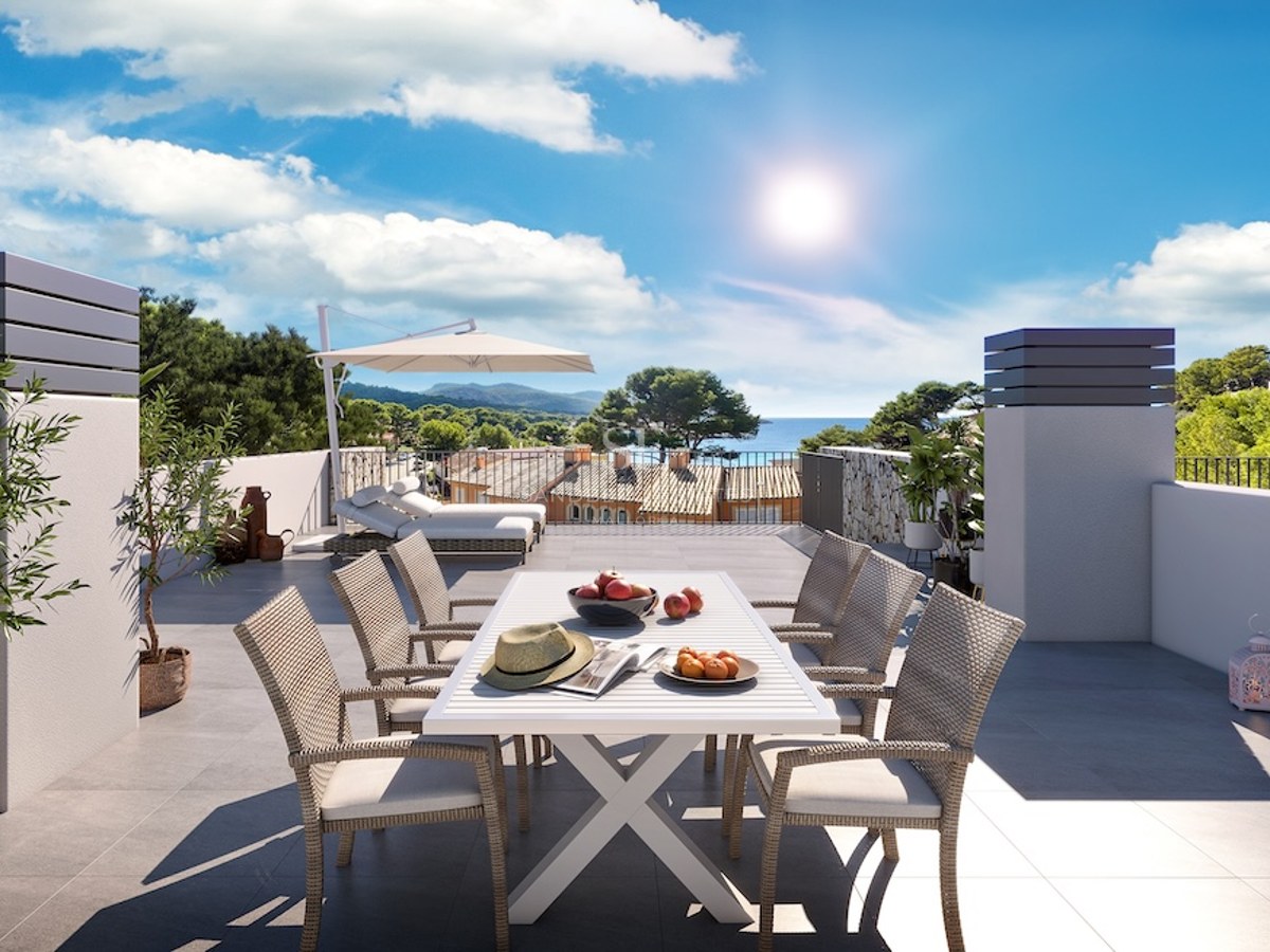 Terraza soleada con comedor exterior, tumbonas y vistas panorámicas al mar y las colinas costeras.