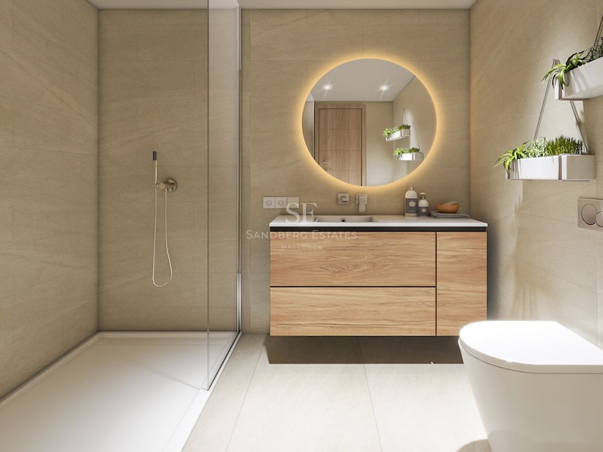 Baño moderno con ducha de cristal, mueble de madera, espejo redondo retroiluminado y plantas decorativas.