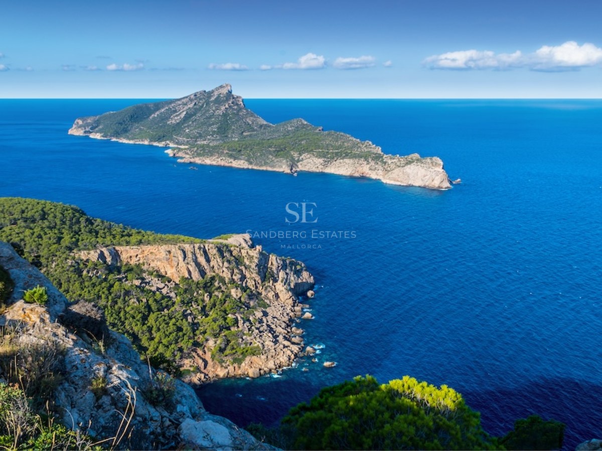 Vista elevada de la costa rocosa de Mallorca con la isla Dragonera sobre el mar Mediterráneo azul profundo.