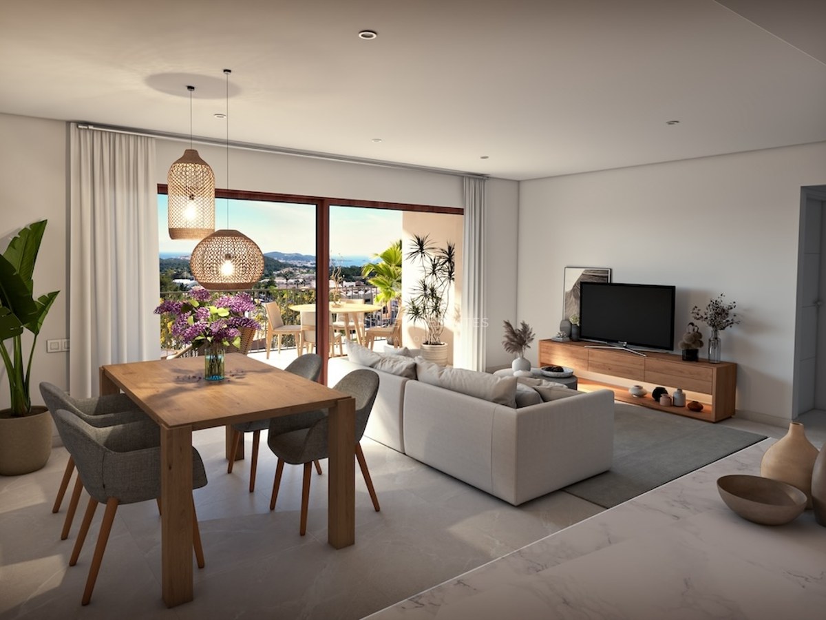 Bright open living room with a grey sofa, wooden dining table, and large glass doors opening to a scenic balcony view.