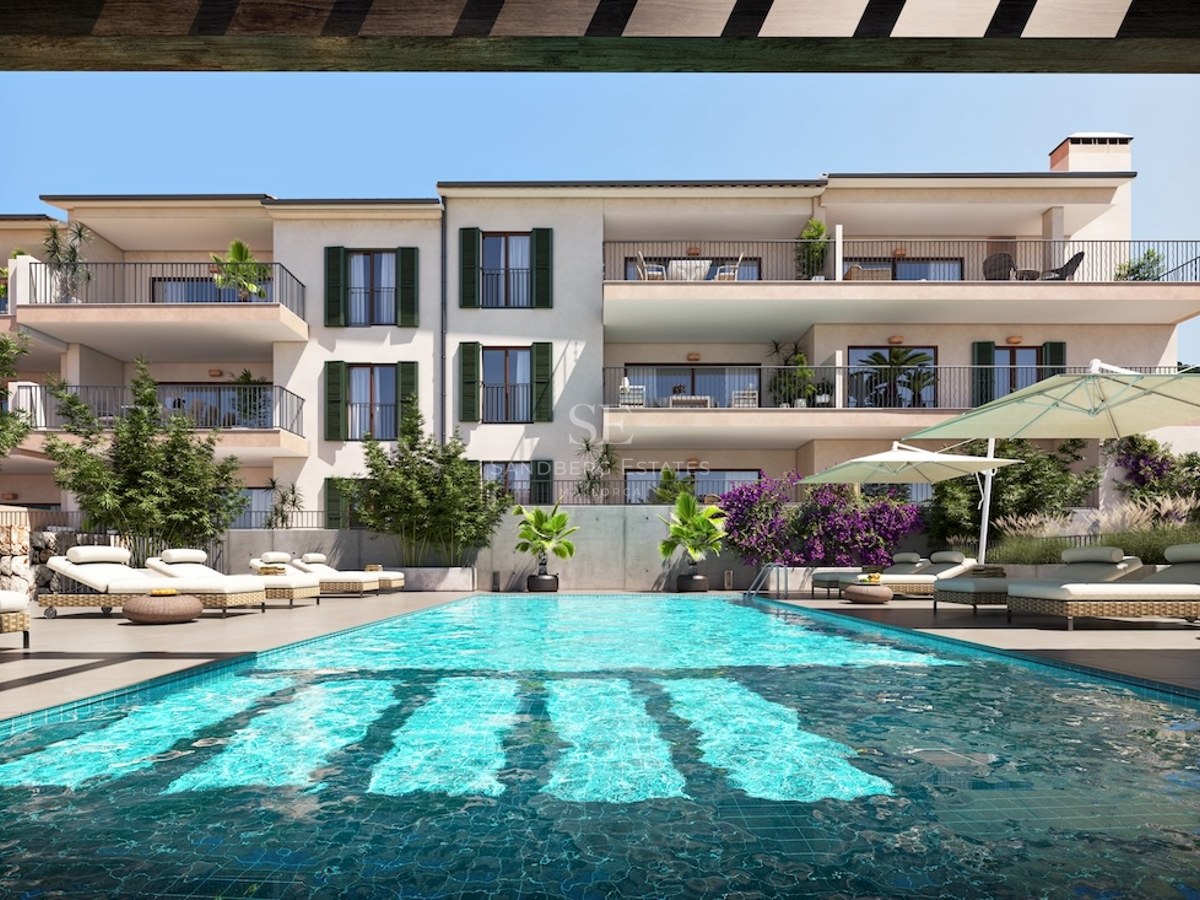 Outdoor swimming pool with sun loungers in front of a modern Mediterranean building with balconies and green shutters.
