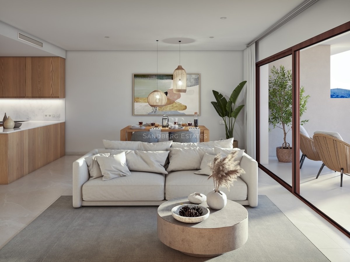 Bright open-plan living room with white sofa, wooden kitchen, and large sliding doors leading to a terrace.