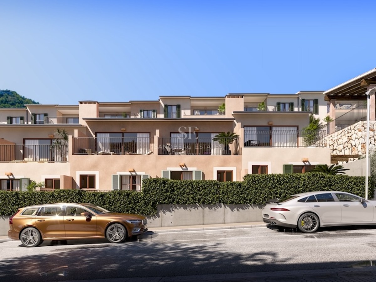 Modern apartment building with balconies, stone walls, and luxury cars parked on the street under a clear blue sky.