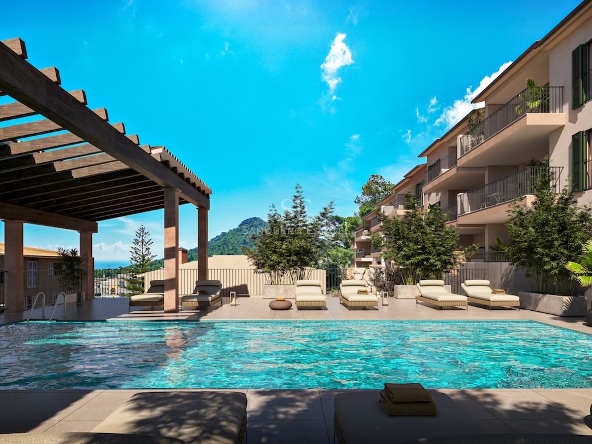Turquoise swimming pool with sun loungers under a wooden pergola overlooking mountains and the sea under a blue sky.