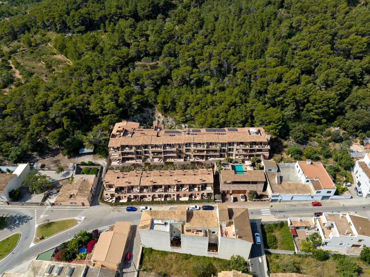 Vista de pájaro de un complejo de apartamentos con techos de terracota junto a un frondoso bosque verde.