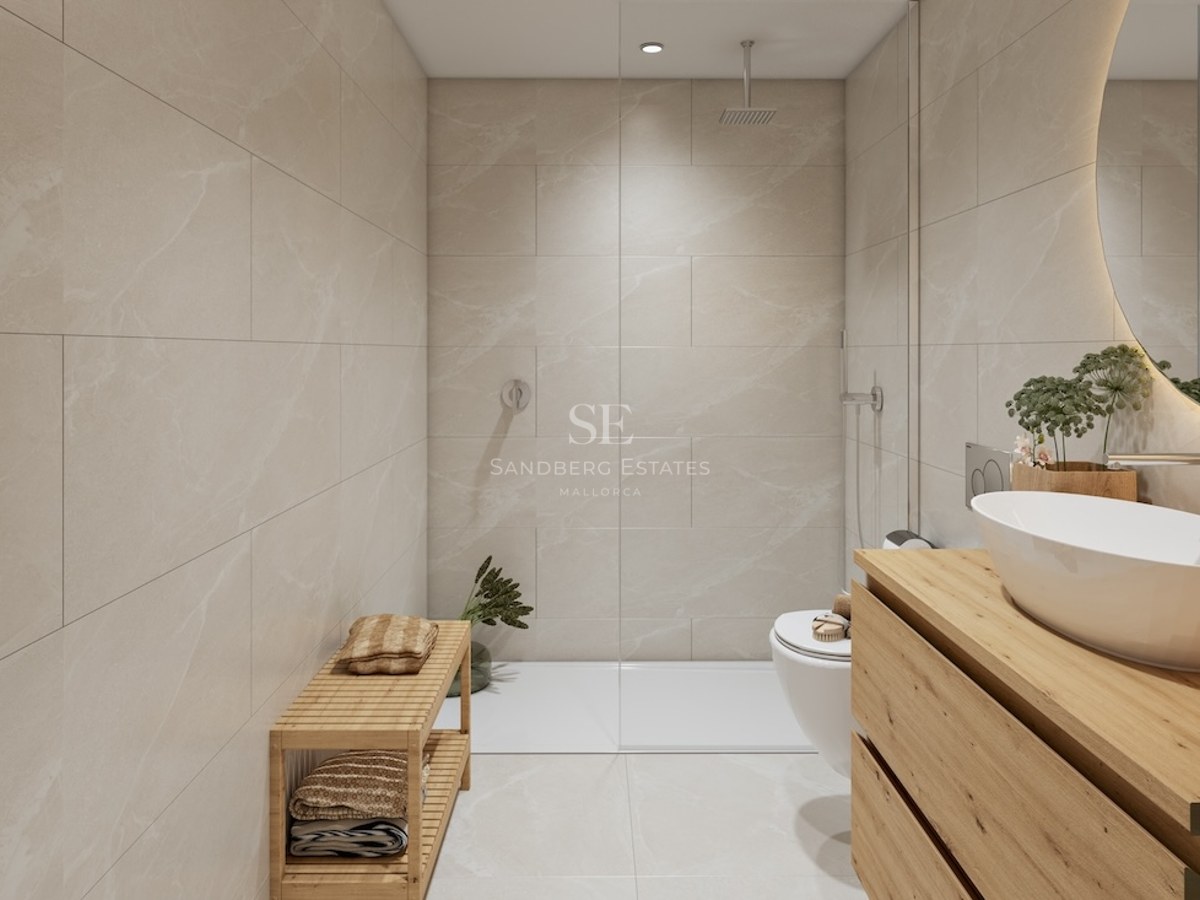 Baño moderno con azulejos beige, ducha de cristal, mueble de madera, lavabo blanco y espejo retroiluminado.