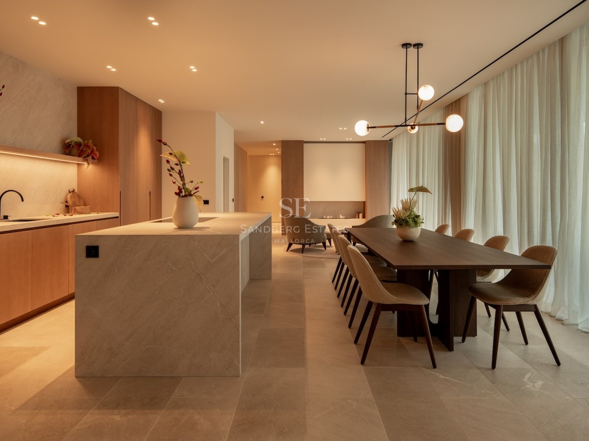 A contemporary open-plan dining room and kitchen featuring a marble island, dark wood table, and warm designer lighting.