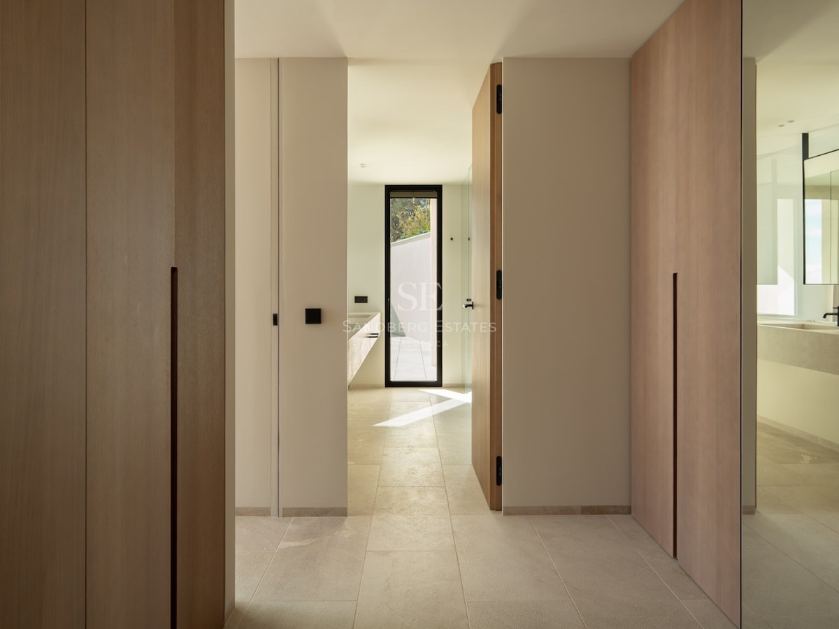 Hallway with floor-to-ceiling light wood wardrobes leading to a bright bathroom.