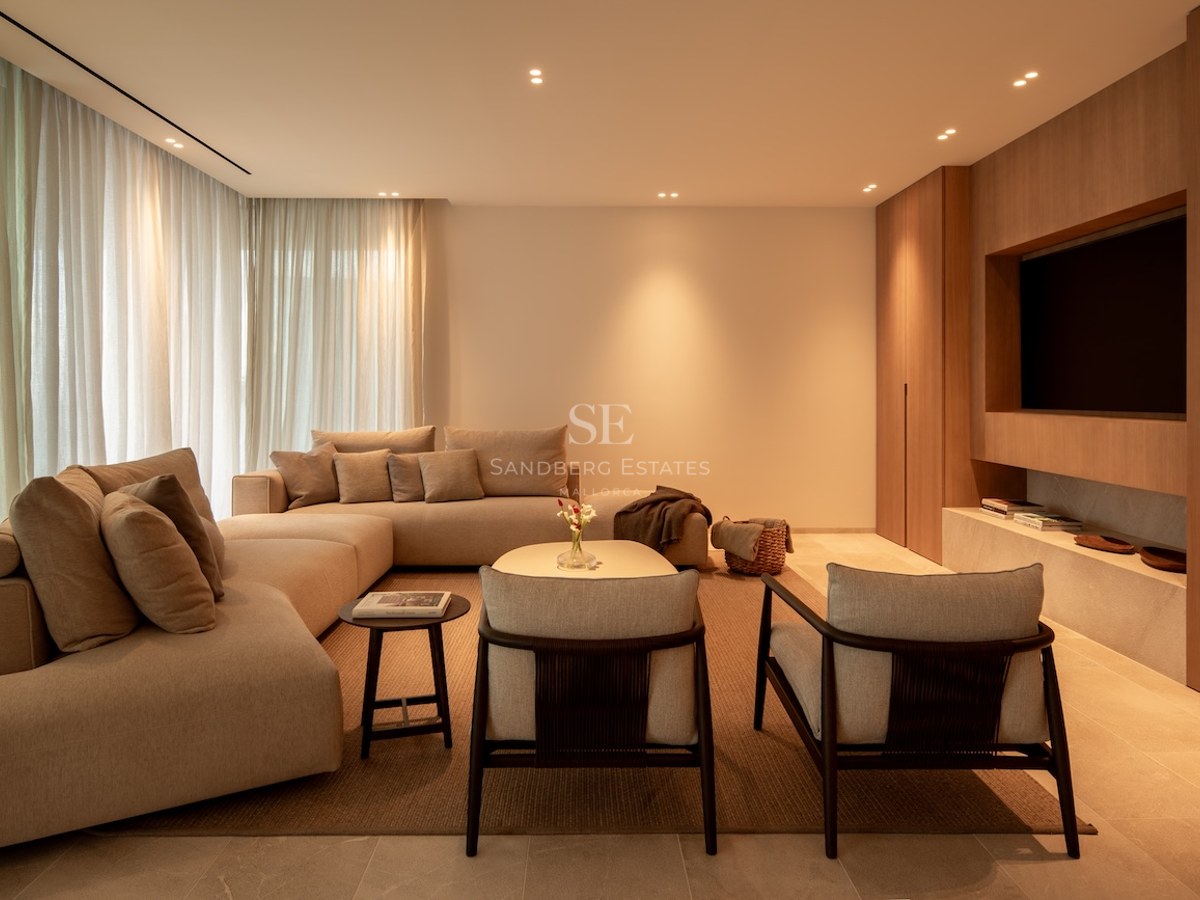 Elegant living room with large beige modular sofa, wooden wall paneling with integrated TV, and warm lighting.
