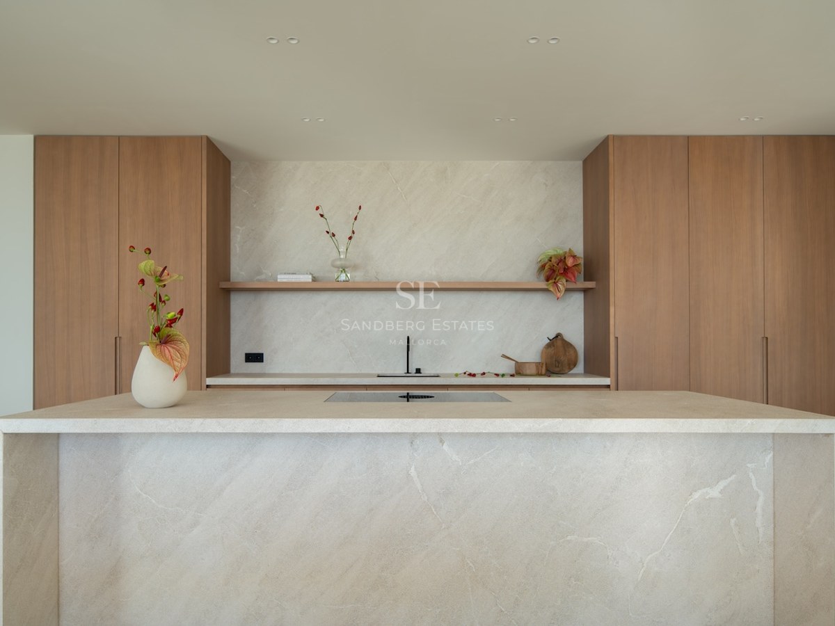 Modern kitchen featuring a large beige stone island, natural wood cabinets, and a matching stone backsplash.