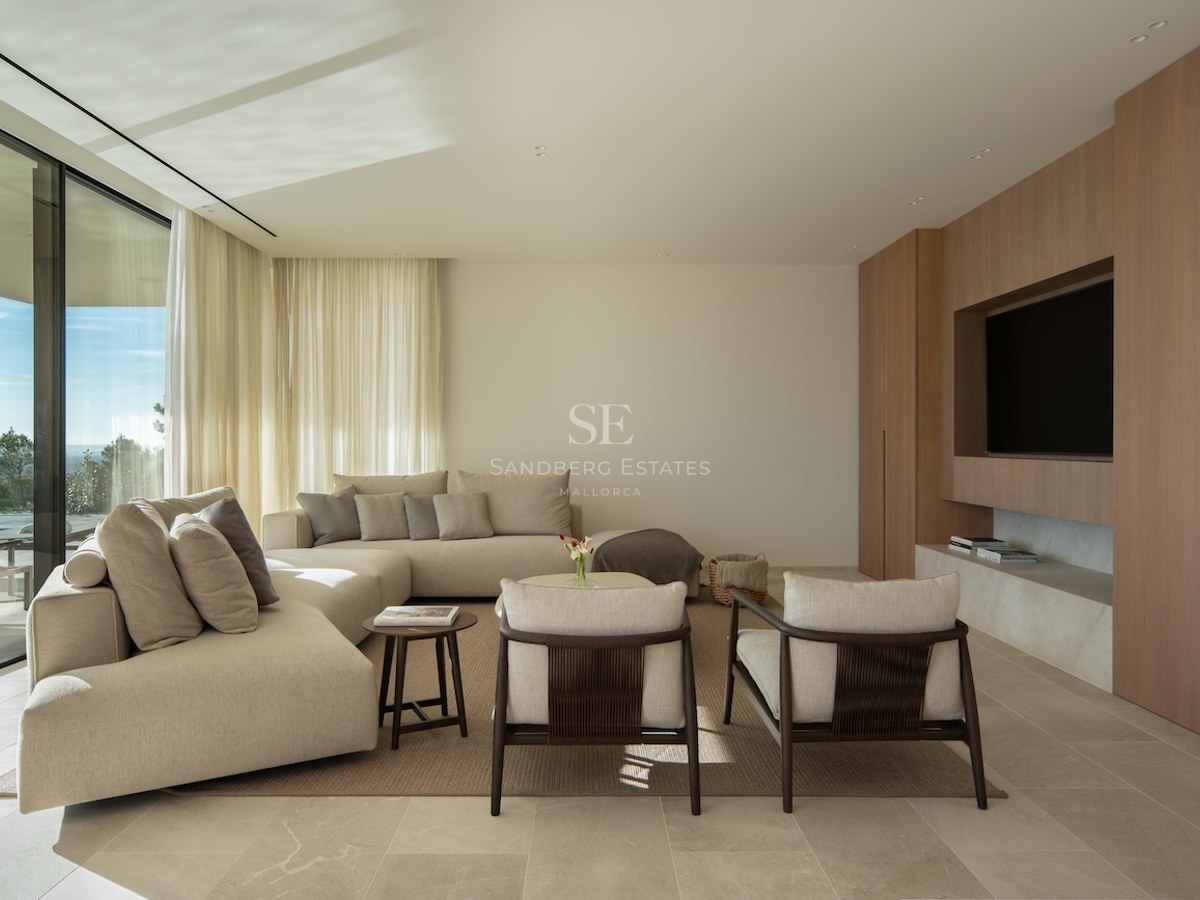 Modern living room with a beige sectional sofa, wood paneled TV wall, and floor-to-ceiling windows with a scenic view.