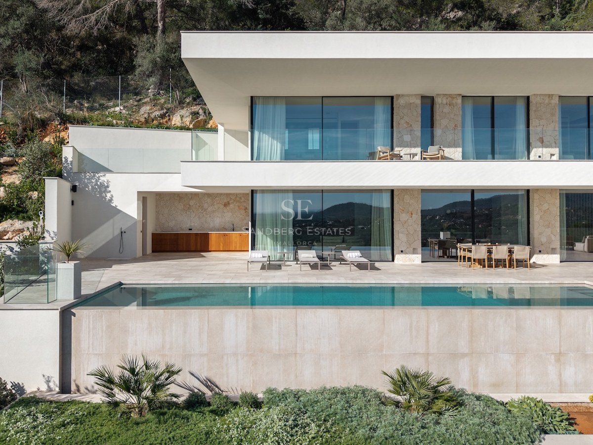 Modern two-story villa with a turquoise infinity pool, stone walls, large glass windows, and a sunny terrace.