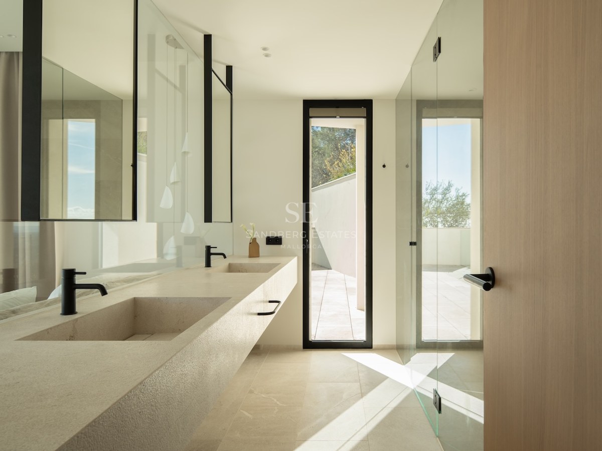 Modern bathroom featuring a long stone double vanity with black faucets, large mirrors, and natural light from a window.