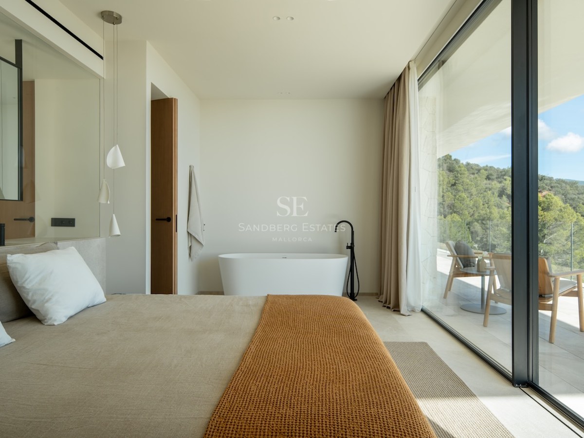 Luxury bedroom with a freestanding bathtub next to large glass doors overlooking a forest and private terrace.