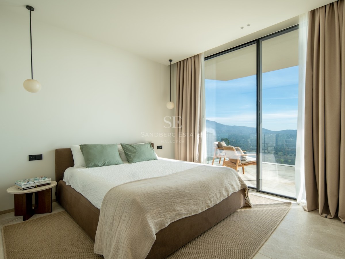 Modern bedroom with floor-to-ceiling windows leading to a terrace overlooking mountains.