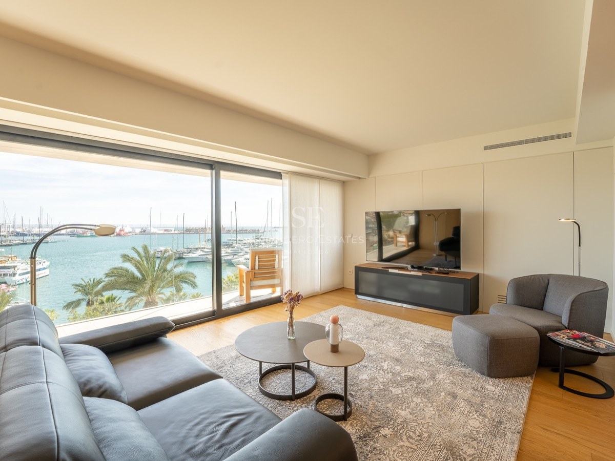Salon moderne avec canapé en cuir noir et grandes baies vitrées donnant sur une marina ensoleillée.