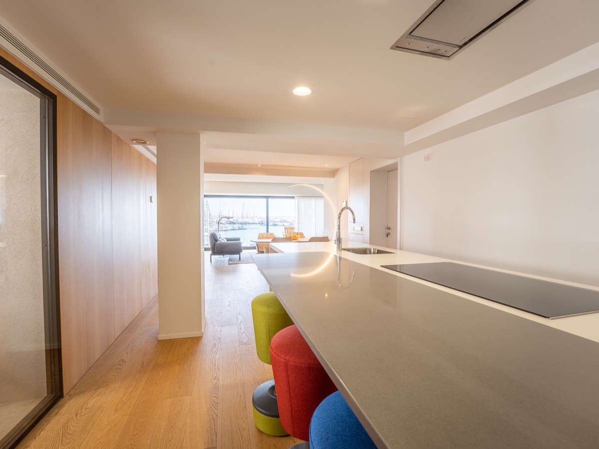 Îlot de cuisine avec tabourets colorés menant à un salon lumineux avec vue sur le port.