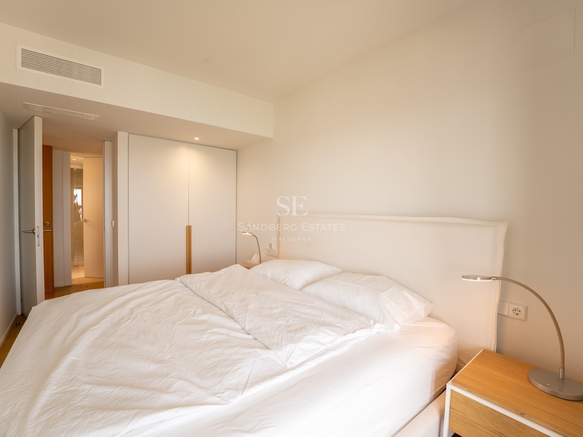Chambre lumineuse avec grand lit, draps blancs, placard intégré et table de chevet en bois.