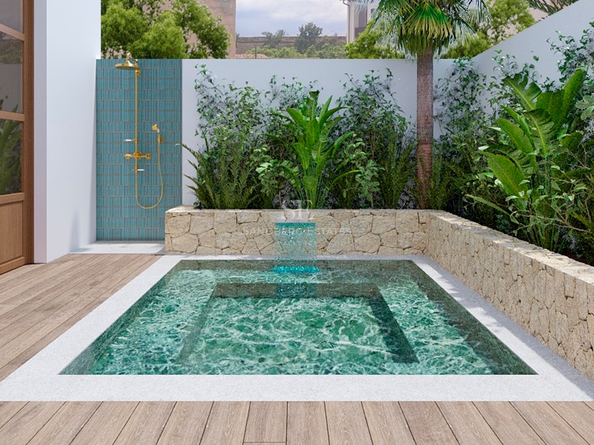 Liten turkos pool med vattenfall, omgiven av stenmurar och växter, bredvid en utomhusdusch i mässing.